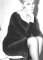 Wendy Richard sitting on a high stool, wearing a dark velour dress.