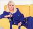 Wendy Richard, wearing royal blue, reclining on a yellow couch
