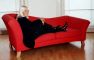 Wendy Richard, dressed in black, reclining on a red couch