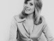 Wendy Richard sits face-on, on top of a couch, wearing only a long shirt