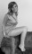 Wendy Richard sits sideways on top of a couch, wearing only a long shirt